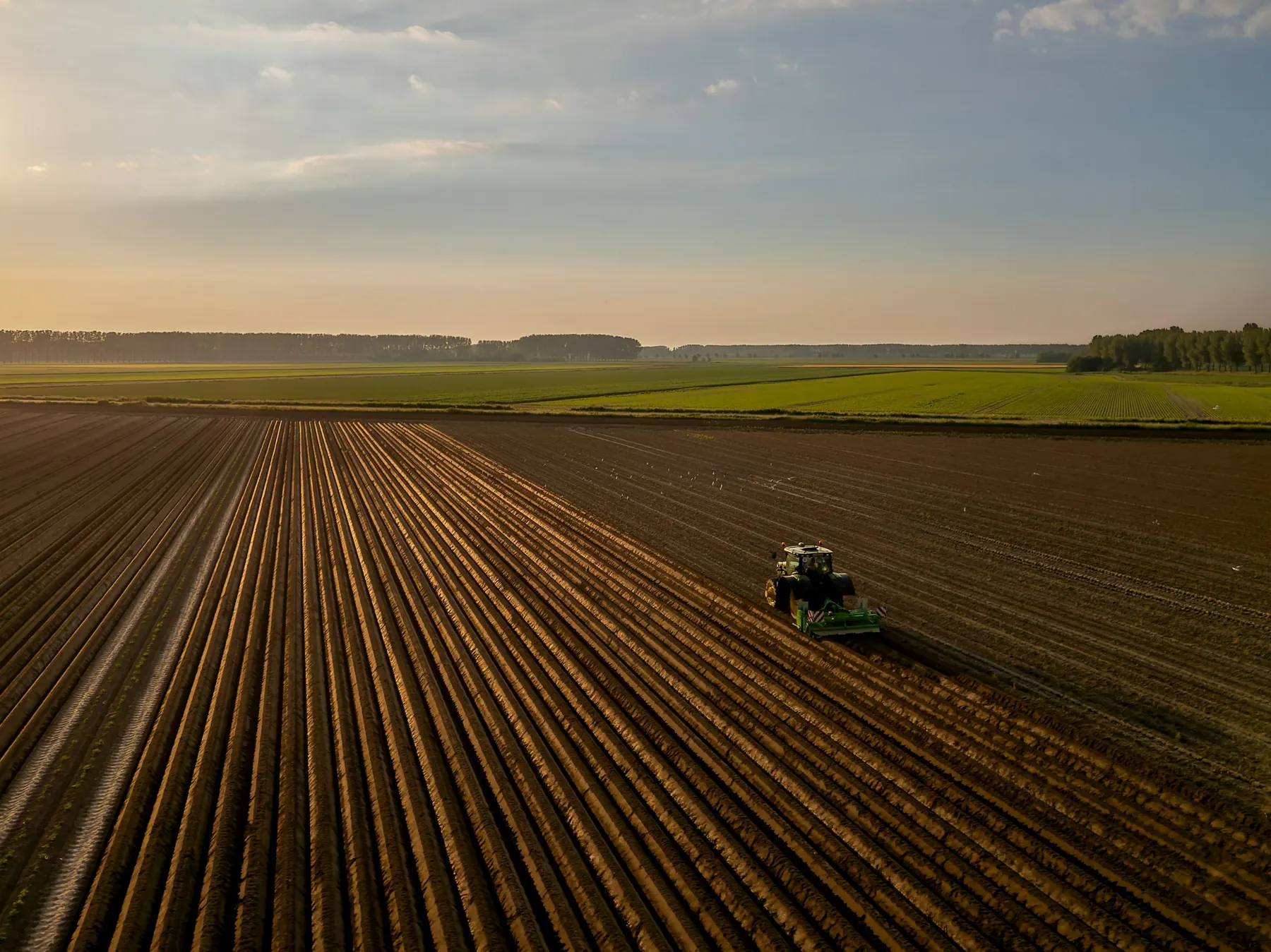 Un tracteur dans un champ labouré au coucher du soleil